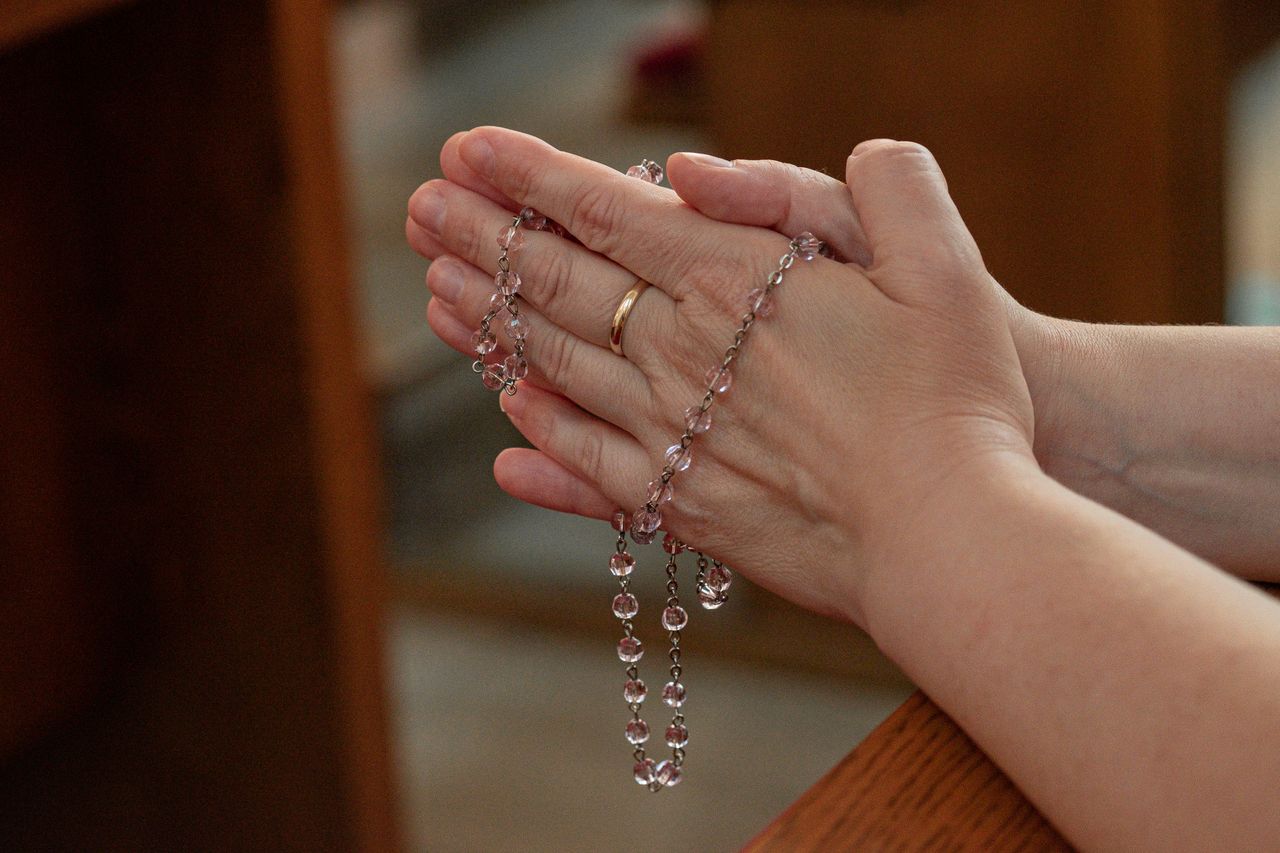 services-04 Close-up of hands holding rosary beads in a prayerful gesture.