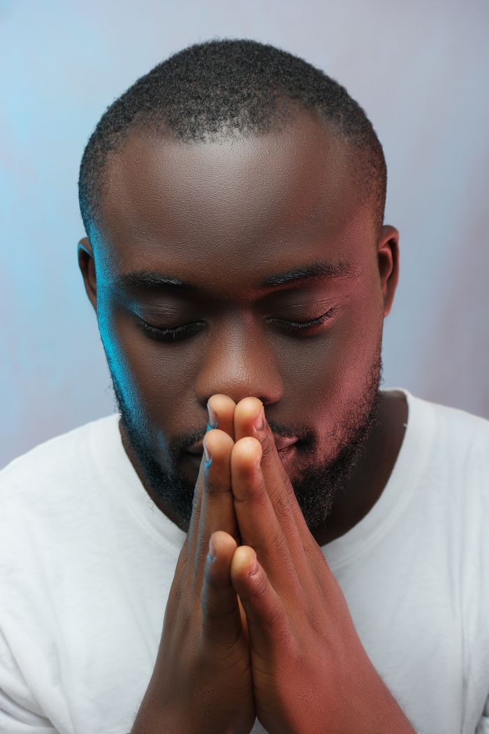 Close-up portrait of a man with eyes closed and hands clasped in prayer.